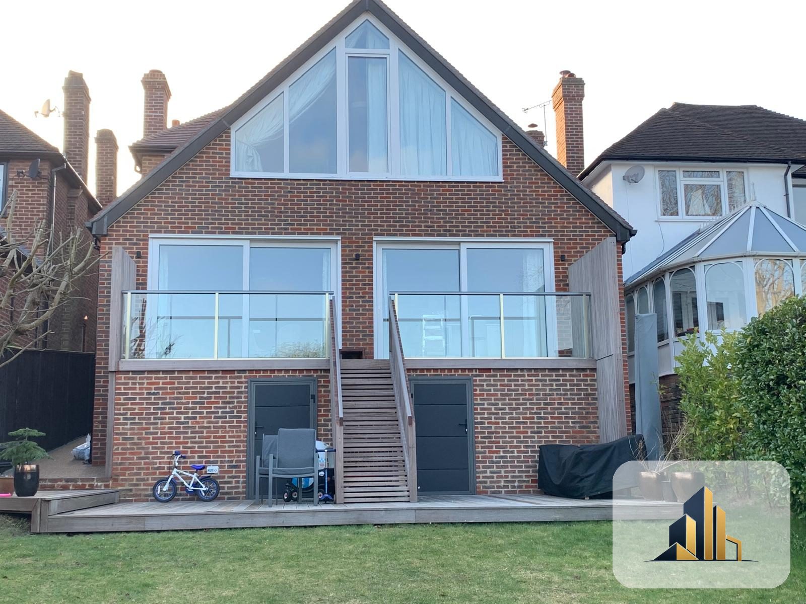Completed rear of the Banstead house with apex feature glazing, glass-balustrade balconies and timber decking