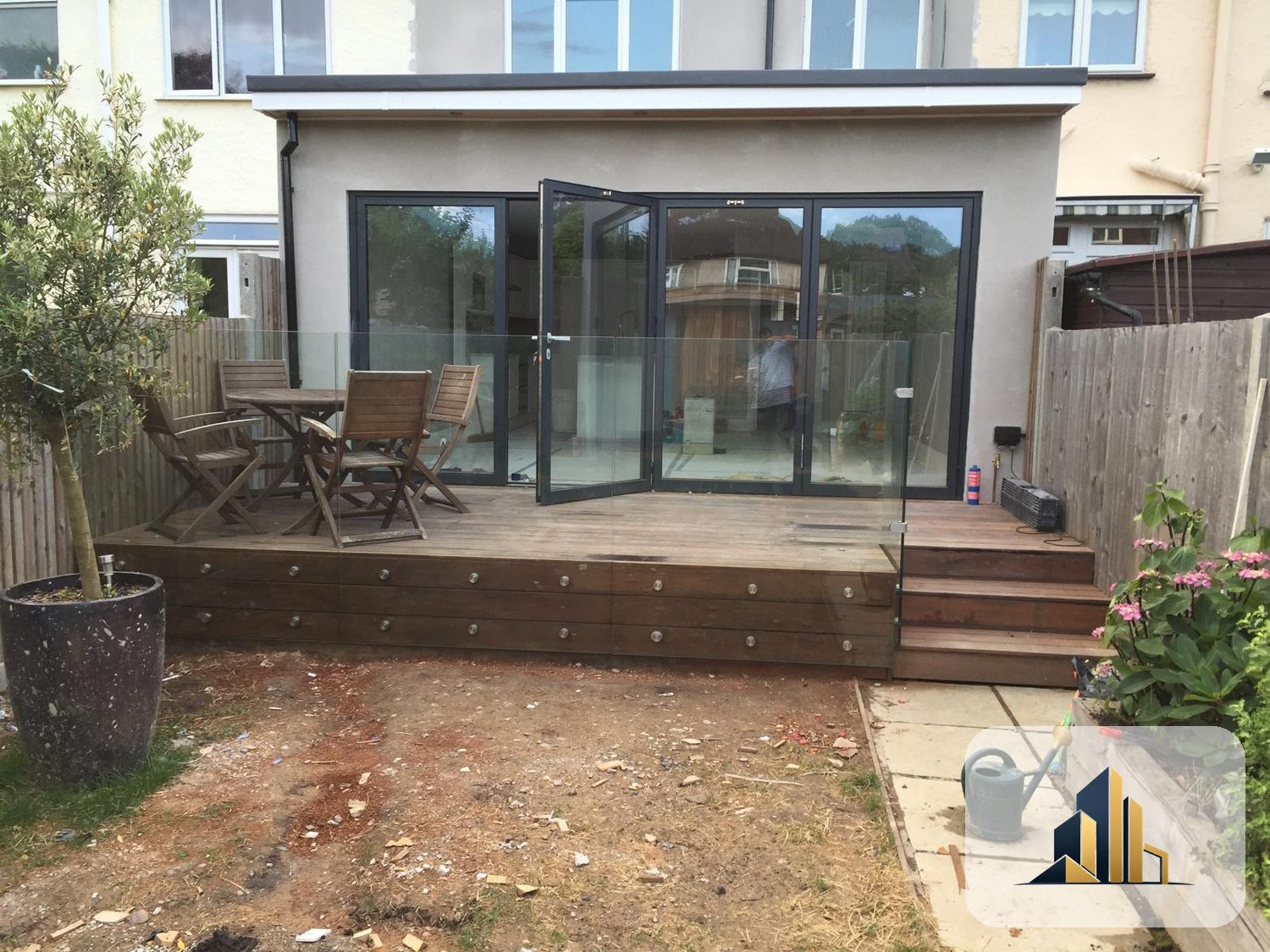 Finished Motspur Park rear extension with bifold doors open onto a raised timber deck with glass balustrade