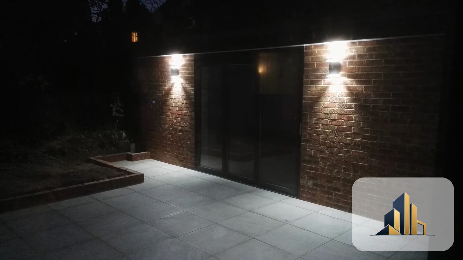 Finished garden room at night with full-height bifold doors, exposed brickwork and exterior lighting, Raynes Park